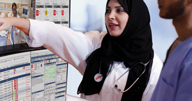 a woman wearing a black head scarf and stethoscope pointing at a computer screen